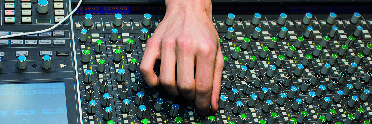 A hand turns one of a hundred dials on a sound desk